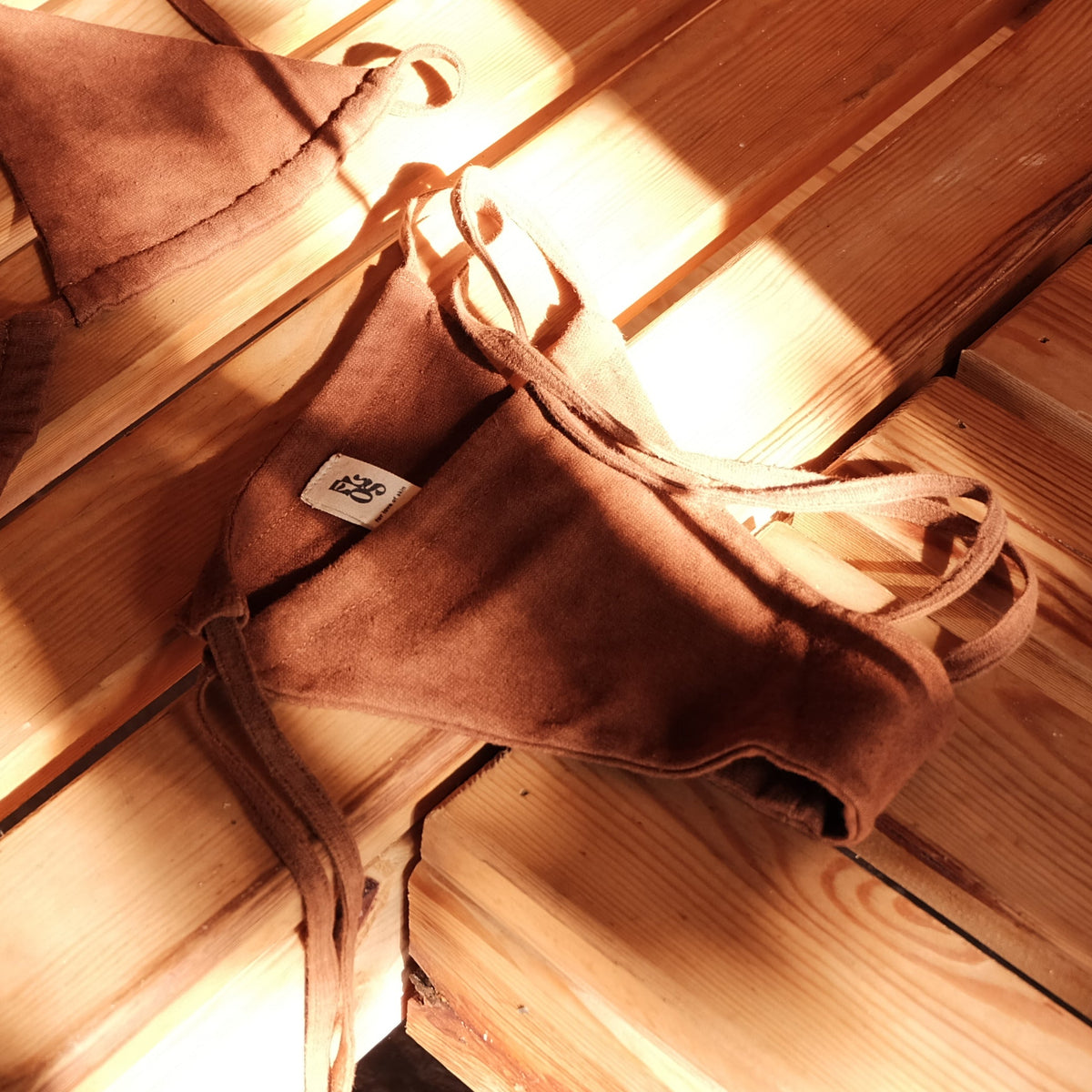 A pair of brown bikini bottoms with tie straps, laid out in a sauna in warm, sunlit shadows.