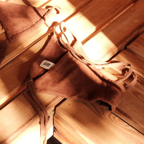 A pair of brown bikini bottoms with tie straps, laid out in a sauna in warm, sunlit shadows.