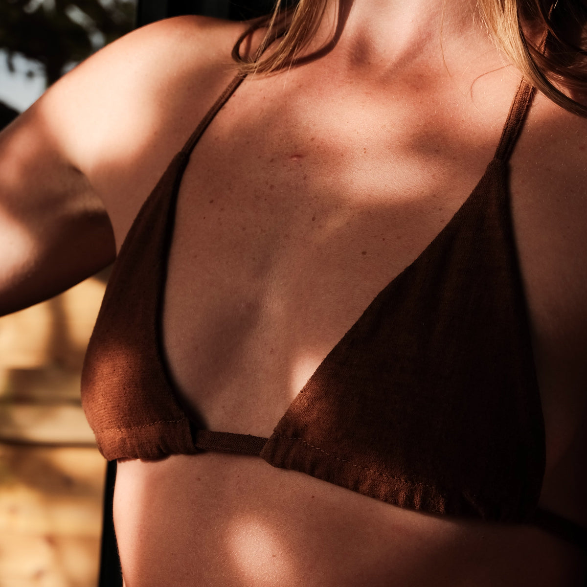 Close-up of a person wearing a dark brown triangle bikini top, with warm sunlight and shadows across the skin.
